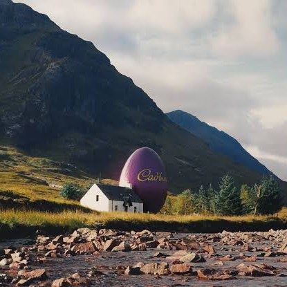 A giant purple Cadbury egg beside a white cottage in a Highland valley, by a rocky river