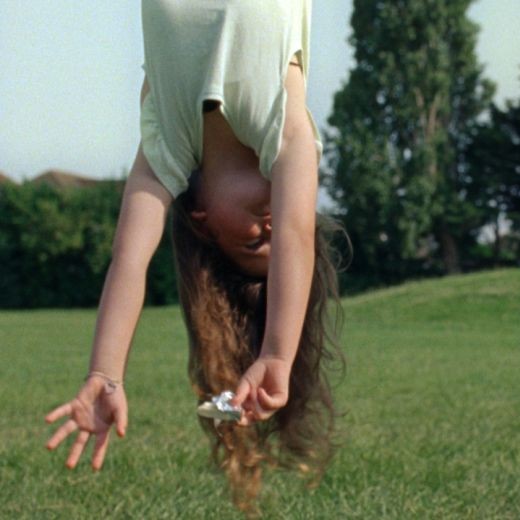 A girl hanging upside down on the grass, holding a Dairylea triangle