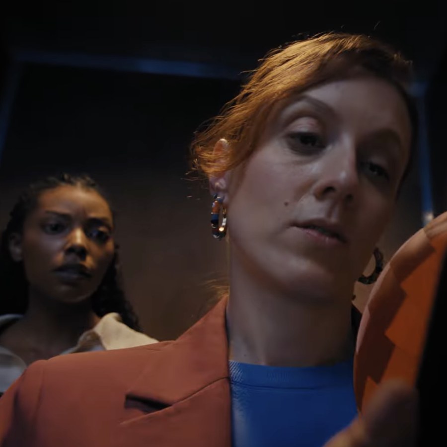 A woman looks down at her phone while another watches from behind