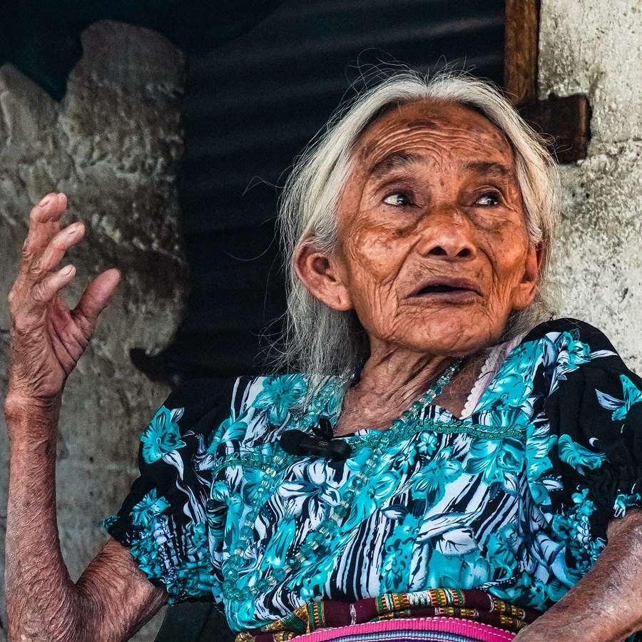 An elderly woman in a blue floral blouse mid-story, from the Lake Atitlán documentary