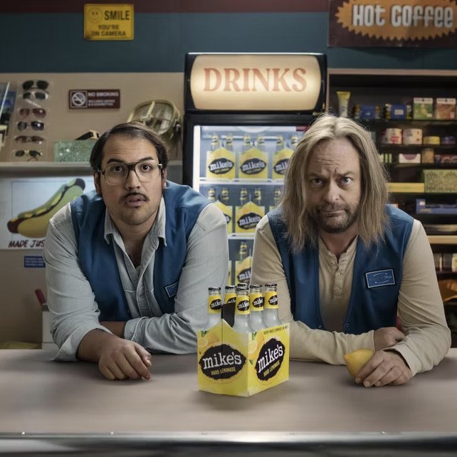 Two shop clerks behind a counter with a six-pack of Mike's Hard Lemonade