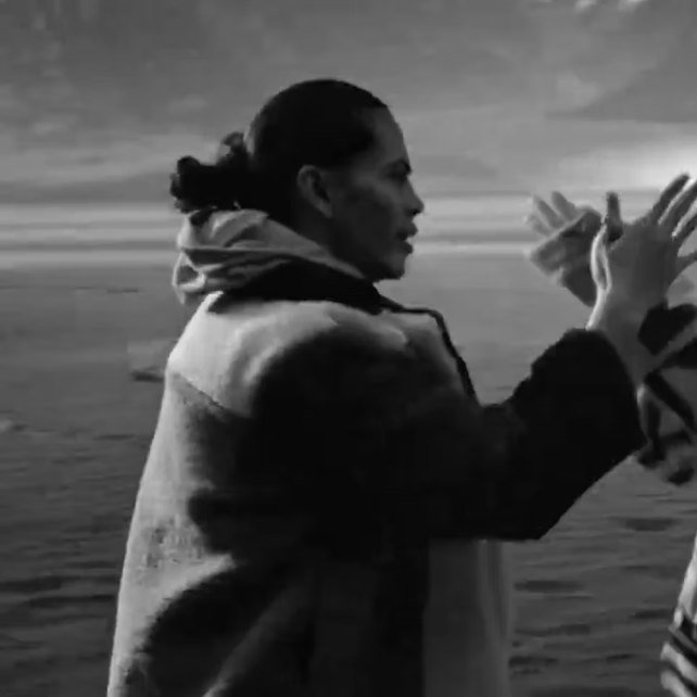 Black-and-white film still of a woman applauding by the water